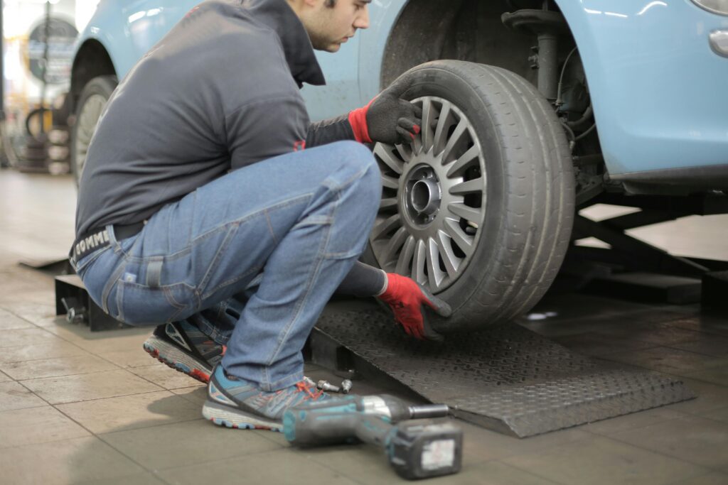 pexels-photo-3806249-3806249 Mechanic changing a car tire indoors, using tools for vehicle maintenance.